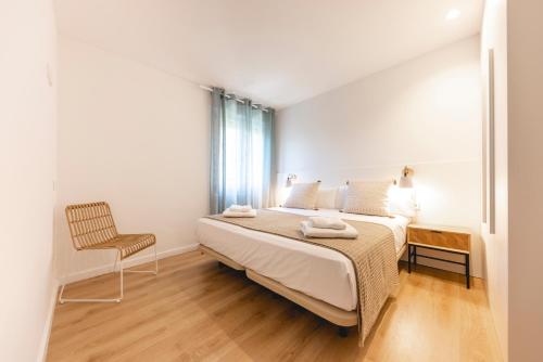 ein weißes Schlafzimmer mit einem Bett und einem Stuhl in der Unterkunft Bravissimo Sirenes, 2-bedroom apartment in Girona