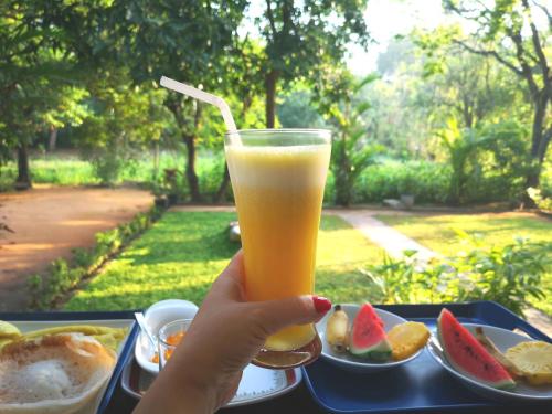 una persona che tiene in mano un bicchiere di succo d'arancia con un piatto di frutta di The Cattleya Guest House Sigiriya a Sigiriya