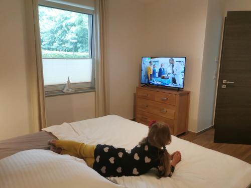 a little girl laying on a bed watching tv at Hafenkoje Anita in Zinnowitz