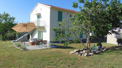 a small white house with a table and an umbrella at Il Giardino di Marzo Guest House in Monti di Licciana Nardi