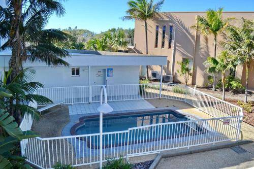 una piscina frente a una casa con palmeras en Ocean Shores Apartment 13, en South West Rocks
