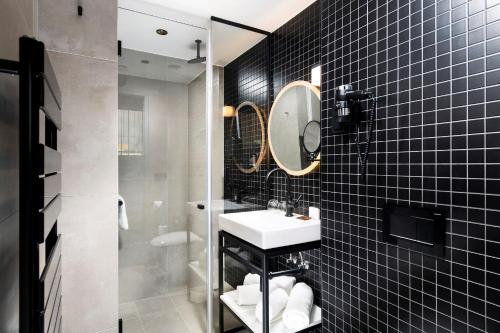 a black tiled bathroom with a sink and a mirror at Three Corners Downtown Hotel in Budapest