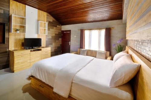 a bedroom with a large white bed and a television at Jero Delod Guesthouse in Tabanan