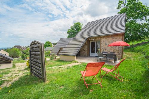 Village de gîtes Les Chalets de l'Aubrac في أومونت أوبراك: منزل به كرسيين ومظلة حمراء