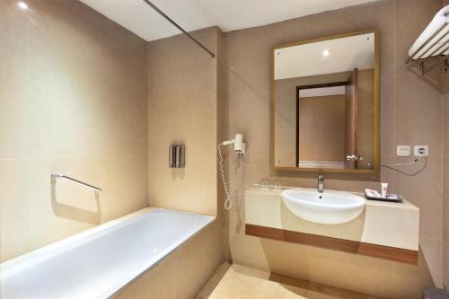 a bathroom with a tub and a sink and a mirror at Prima In Hotel Malioboro in Yogyakarta