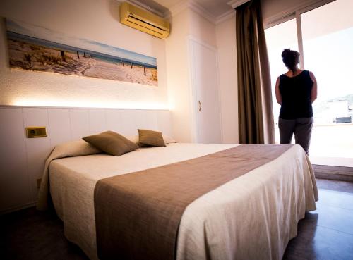 a woman standing in a bedroom looking out the window at Hotel Claramar in Platja  d'Aro