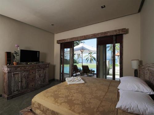a bedroom with a bed and a television and a patio at Villa Rumah Pantai Bali in Selemadeg