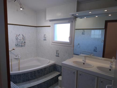 een badkamer met 2 wastafels, een bad en een raam bij Gîte climatisé les hirondelles in Pons