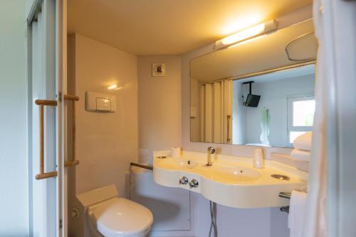 La salle de bains est pourvue d'un lavabo, de toilettes et d'un miroir. dans l'établissement Hôtel Cerise Auxerre, à Monéteau