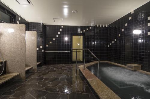 a bathroom with a hot tub with black tiles at Green Rich Hotel Izumo (Artificial hot spring Futamata Yunohana) in Izumo
