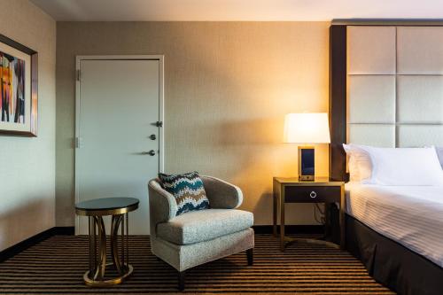 a hotel room with a bed and a chair and a lamp at APA Hotel Woodbridge in Iselin