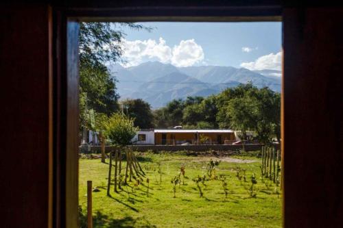 a window view of a field with a house and mountains at Estancia Rio de Arena in Colalao del Valle