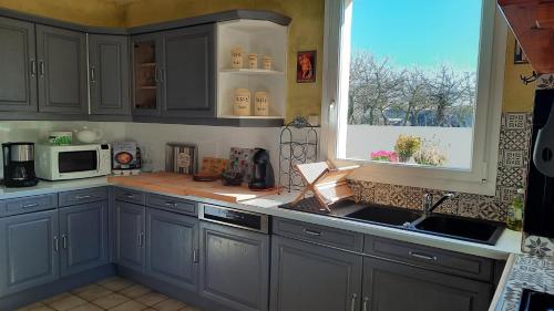 - une cuisine avec des placards gris, une fenêtre et un évier dans l'établissement Gite galets et bois flottés proche mer gold beach meublé de tourisme 4 étoiles, à Meuvaines