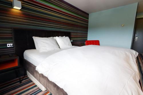 a bedroom with a large white bed with a striped wall at Village Hotel Newcastle in Newcastle upon Tyne