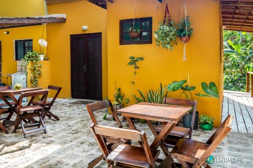a patio with tables and chairs in front of a yellow wall at Chalés da Libélula in Ilhabela
