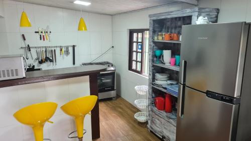 a kitchen with a stainless steel refrigerator and yellow stools at Casa Paúba 80m do Mar in Maresias