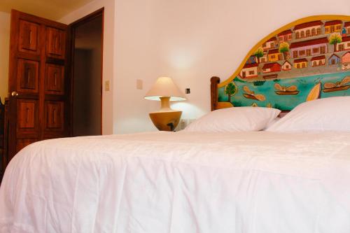 a bedroom with a white bed with a painting on the wall at Casa Rosa Mexicano in Oaxaca City