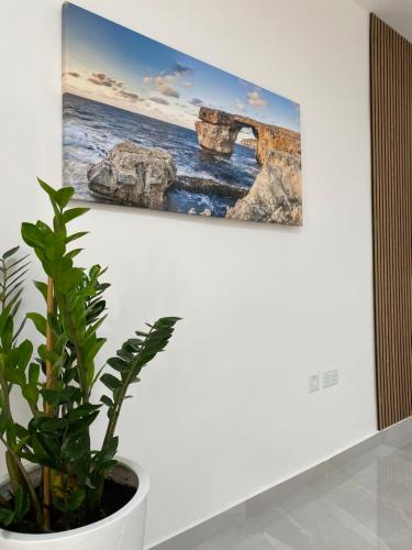 a painting hanging on a wall next to a plant at Seaside Apartment in Gzira in Il-Gżira