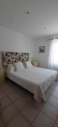 Cette chambre blanche comprend un grand lit blanc et une fenêtre. dans l'établissement LA CIGALE ARGELES - MADELOC, à Plage dʼArgelès