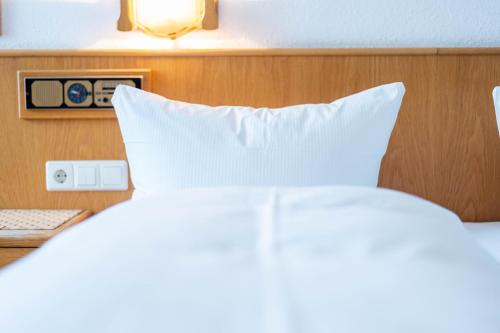 a bed with white pillows and a table with a clock at Hotel am Römerplatz in Ulm