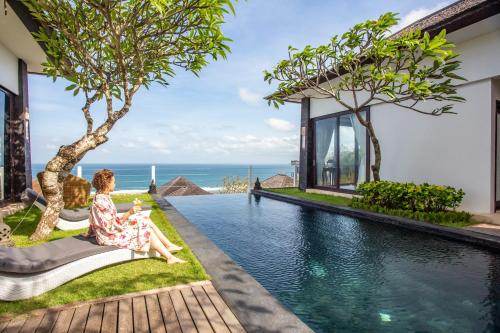 a woman sitting on a bench by a pool in a villa at Nusa Dua Ocean Cliff Dream in Ungasan