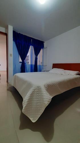 a bedroom with a white bed with a blue window at Apartamentos Turisticos EL ZIPA in Zipaquirá