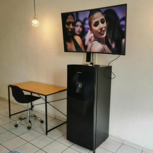 a black refrigerator with a table and a tv on the wall at Lovely studio apartment with balcony AC & wi-fi, minutes from downtown! in Zihuatanejo