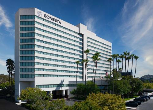 a large white building with palm trees in a parking lot at Sonesta Irvine in Irvine