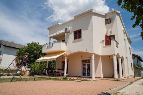 una casa blanca con un parque infantil delante de ella en Apartments by the sea Sukosan, Zadar - 12313, en Sukošan