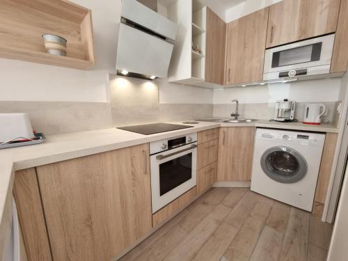 - une cuisine avec des placards en bois et un lave-linge dans l'établissement Charmant T2 avec Terrasse et Jardin Clos à 200m de la Plage - Parking Privé Inclus - FR-1-71-94, à Royan