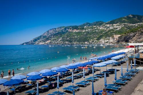 una playa con sombrillas azules y gente en el agua en Capricornio Club, en Maiori