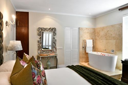 a bedroom with a tub and a bed and a mirror at Le Petit Bijou Boutique Apartments - Solar Power in Franschhoek