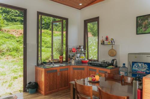 cocina con armarios de madera, mesa y algunas ventanas en Thỏ Non Garden Villa Bảo Lộc, en Bao Loc