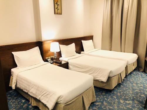 two beds in a hotel room with white sheets at Zaha Al Munawara Hotel in Al Madinah