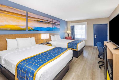 a hotel room with two beds and a flat screen tv at Days Inn & Suites by Wyndham Savannah Midtown in Savannah