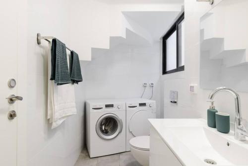 ein weißes Badezimmer mit einer Waschmaschine und einem Waschbecken in der Unterkunft Unique Urban Villa - Live Local with Style in Tel Aviv