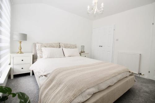 a white bedroom with a large bed and a chandelier at Katie's house in Cumbernauld