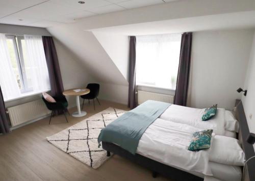 a bedroom with a bed and two windows and a table at Hotel Zuideinde in Nieuwkoop