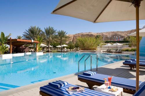 einen Pool mit blauen und weißen Stühlen und einem Sonnenschirm in der Unterkunft Mercure Grand Jebel Hafeet in al-Ain