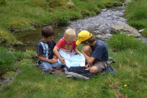 three boys sitting in the grass by a stream with a basket at Waalhof Ferienwohnung Apfelblüte in Silandro