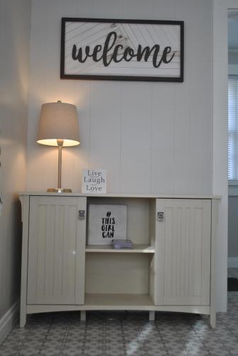 einen Schreibtisch mit einer Lampe und ein Willkommensschild an der Wand in der Unterkunft Black and white cottage; Simple yet stunning. in Joplin