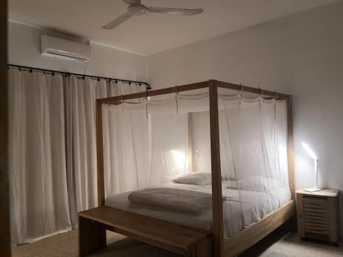 1 dormitorio con cama con dosel y cortinas blancas en Grande maison en bordure de plage en Palmarin