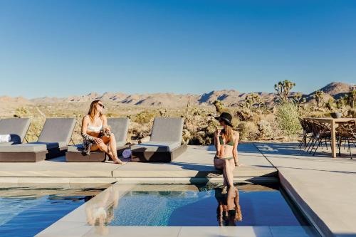 two women sitting on the edge of a swimming pool at Amaru Muru - Luxury Retreat with Pool/Hot Tub/Yoga in Joshua Tree