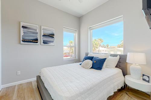 a white bedroom with a bed and two windows at Dolphin Paradise Unit A in South Padre Island