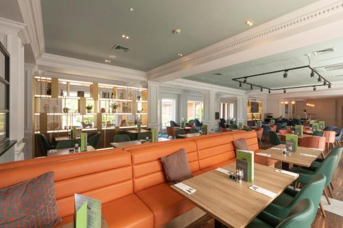 a restaurant with tables and chairs and a long orange couch at Holiday Inn Guildford by IHG in Guildford