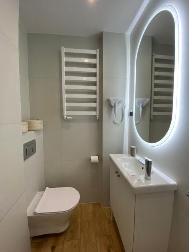 a white bathroom with a toilet and a mirror at La Playa Apartments in Hel