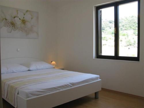 a white bedroom with a bed and a window at Apartment Palit 16356b in Mundanije