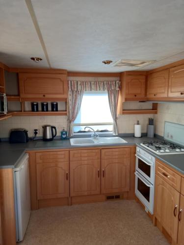 cocina con armarios de madera, fregadero y ventana en Holiday Home, en Forfar