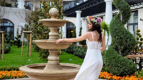 a woman in a white dress standing next to a fountain at Casa di Fiore SPA and Medical Hotel, Mineral Pools & Private Beach in Kranevo