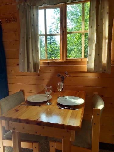a wooden table with two plates and wine glasses at Bakkakot 3 Cozy Cabin In The Woods in Akureyri